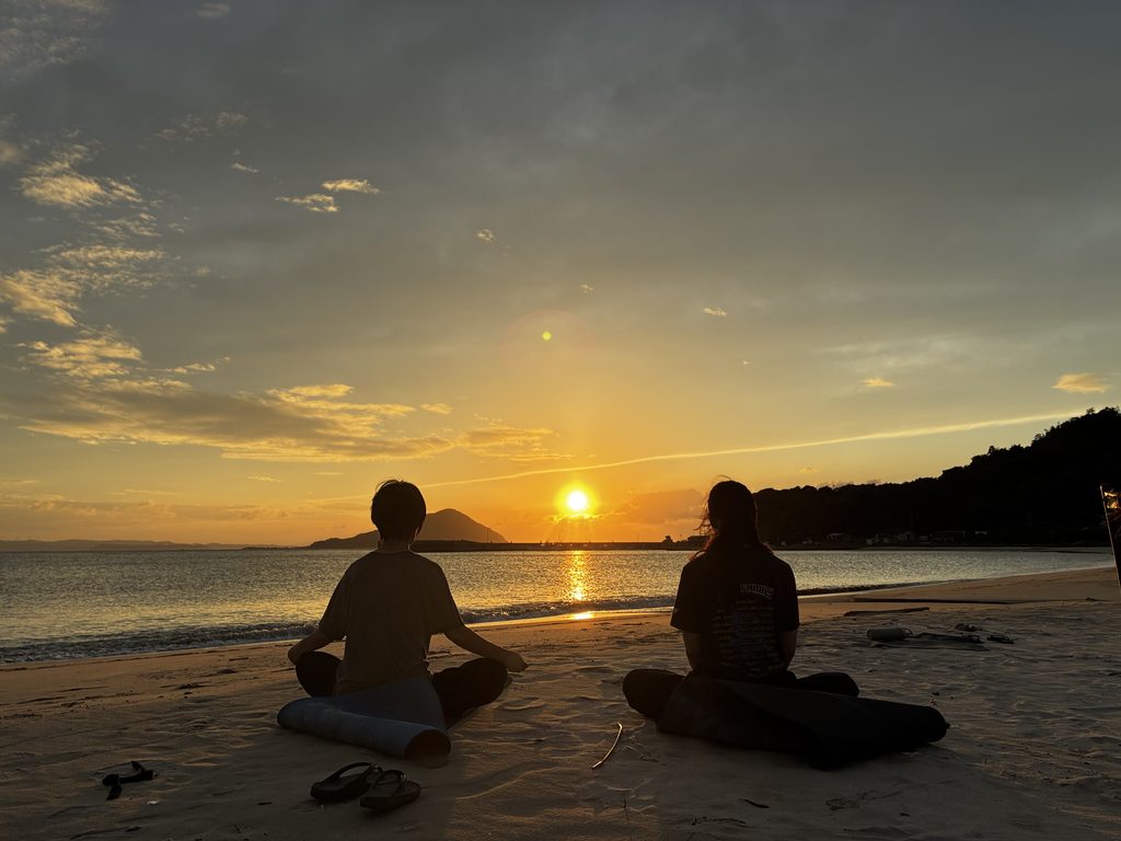 糸島・福の浦の浜辺で夕陽に包まれてヨガを楽しむ二人